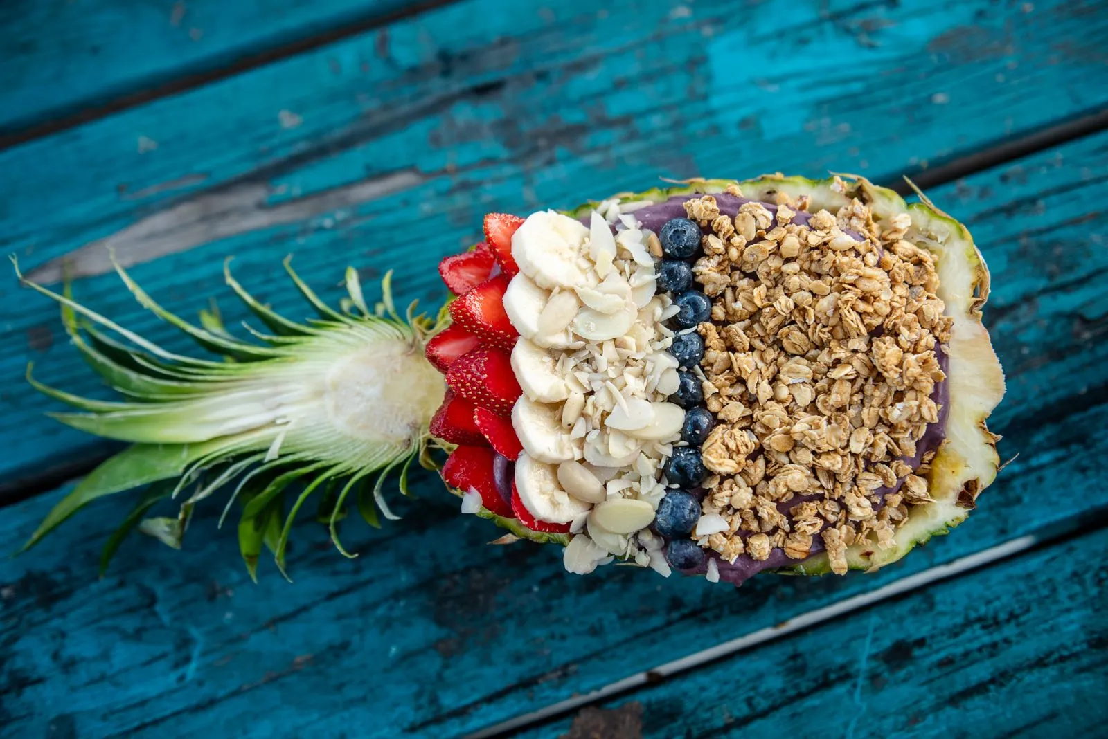 Healthy fruit and granola bowl in a pineapple shell on turquoise rustic table, perfect for a nutritious breakfast.